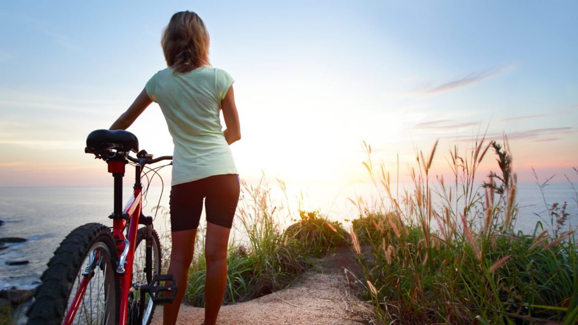 Young,Woman,With,Bicycle,Standing,On,Ground,And,Enjoying,Sunset